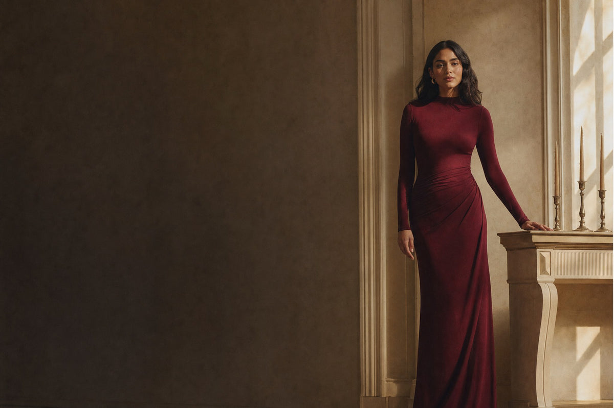 Woman in a wine-red long-sleeve evening gown beside a candlelit console table